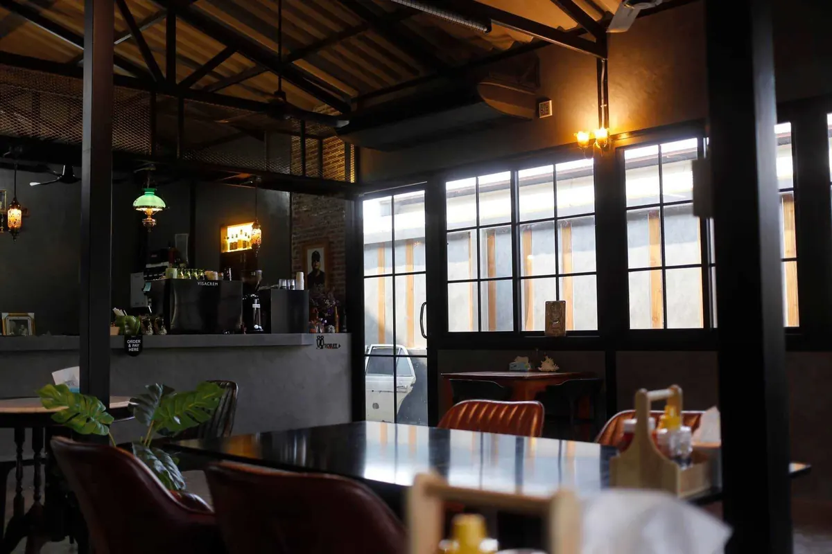 บรรยากาศในร้านช่วงกลางวัน หน้าต่างกรอบเหล็ก โต๊ะไม้ และบาร์กาแฟ